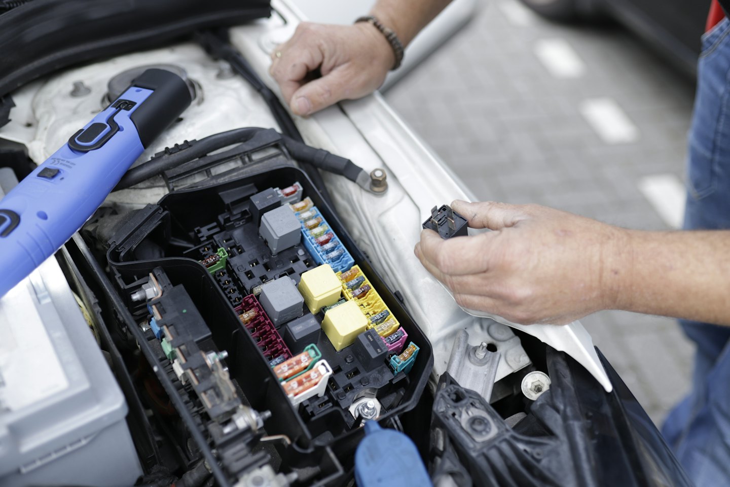 Mechanikove ruky kontrolujúce poistkovú skrinku a elektrické komponenty auta.