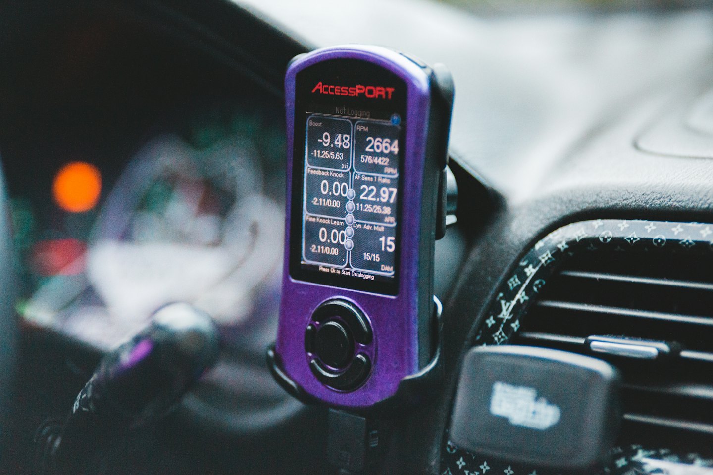 Fialový Cobb AccessPORT tuner zobrazuje údaje o motore na palubnej doske.